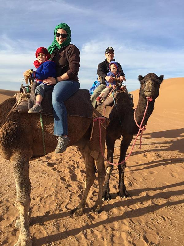 The Newcamp Family rides on Camels with the dunes of Morocco in the background