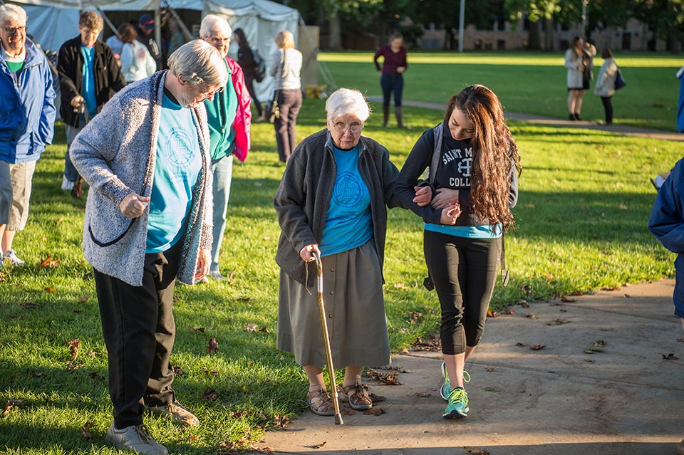 A student helps one of the Sisters walk from the picnic to the volleyball match.