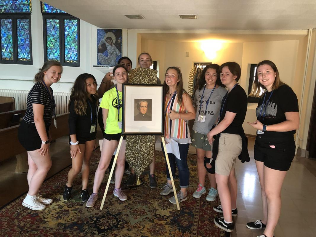 a group of high school students at the Embody Summer Theology Institute at Saint Mary’s College stand around a portrait of Bl. Basil Moreau in the chapel.