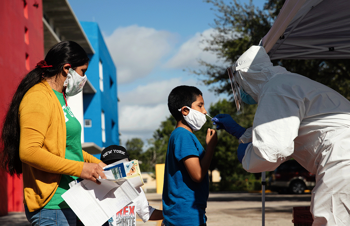 Photo: Kenneth Midoneck, lead community health worker with Healthcare Network, tests Santos Pablo, center, for Covid-19 alongside his mother Juliana Pablo and brother Edvyn Aguilar during a mobile health clinic put on by Healthcare Network in Immokalee, FL on Saturday, Dec. 5, 2020. (Photo by Scott McIntyre for Partners In Health)