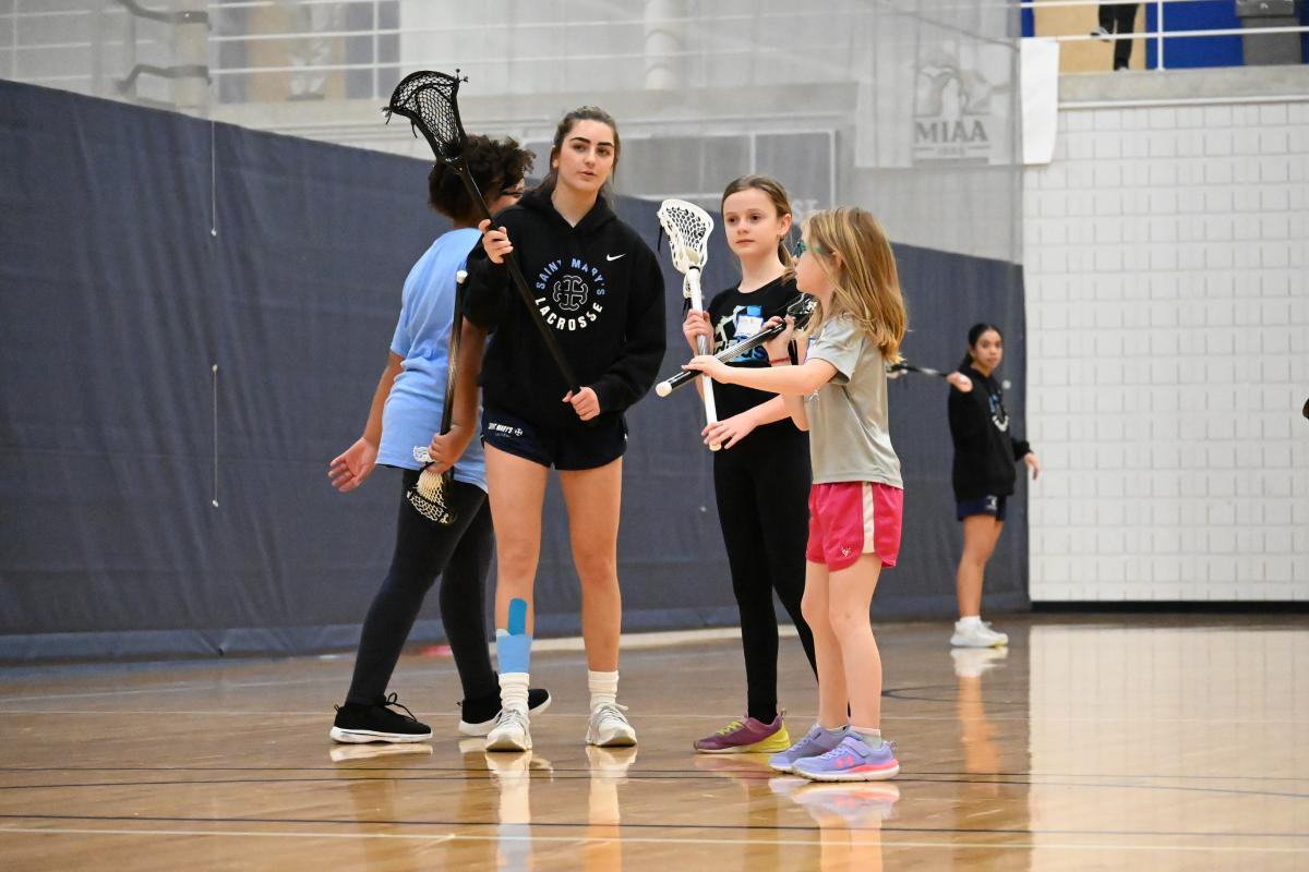 Girls playing lacrosse with student-athletes. 