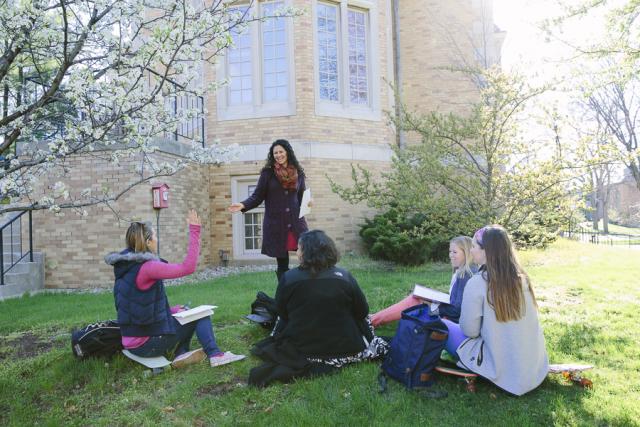 professor calling on student with her hand raised during class outdoors