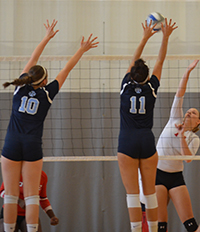 A pair of Belles volleyball players jump to try to block the ball.