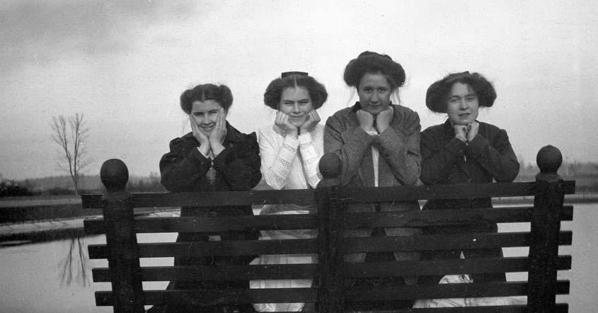 1915 Four students posed on a bench facing the camera by Lake Marian