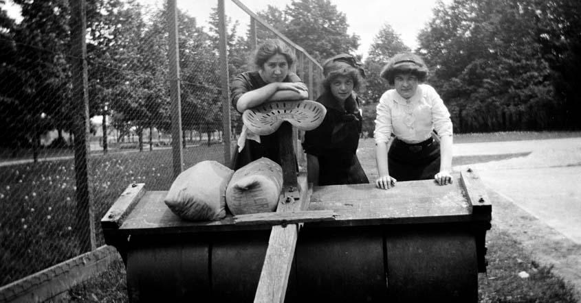 1915 image of three women standing by groundskeeping equipment