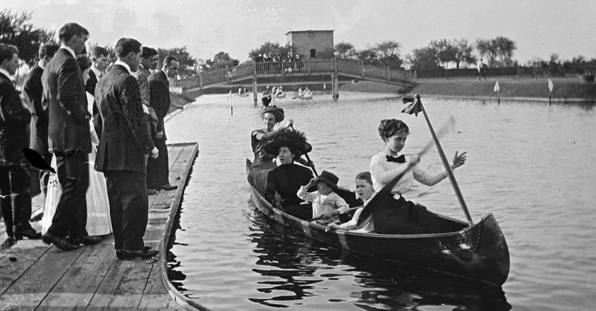 1915 image of women paddling boat in Lake Marian with men standing on dock