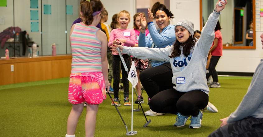 Student athletes works with young camper